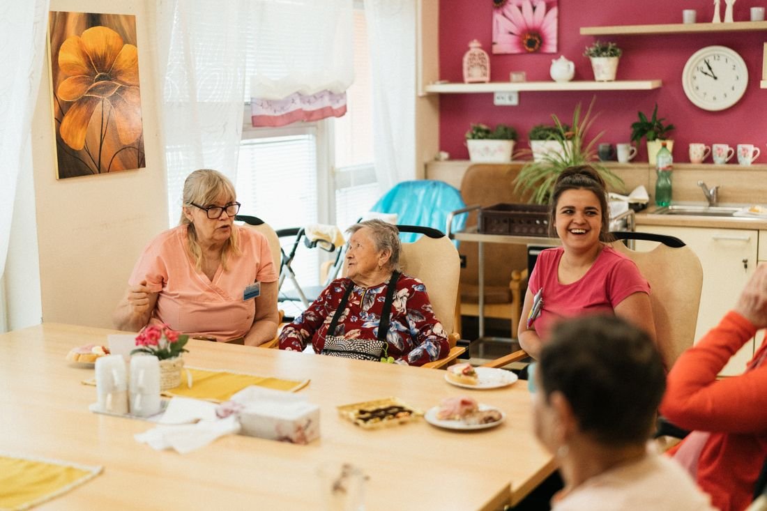 Ältere Menschen und Betreuerinnen beim gemeinsamen Kaffee in der Tagespflege